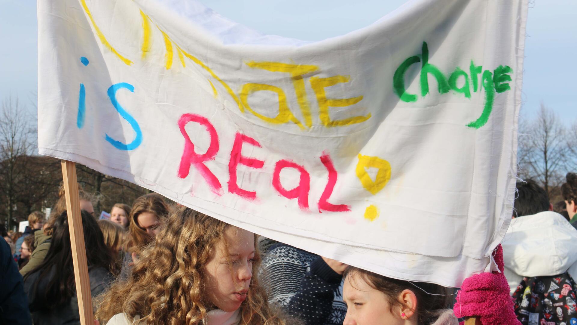 Twee jonge witte kinderen van ongeveer 12 jaar met een spanbord waar op staat 'climate change is real'